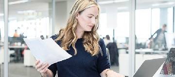 A woman holding a document in one hand and a laptop in the other