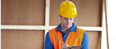 A construction worker holding a pad and writing notes